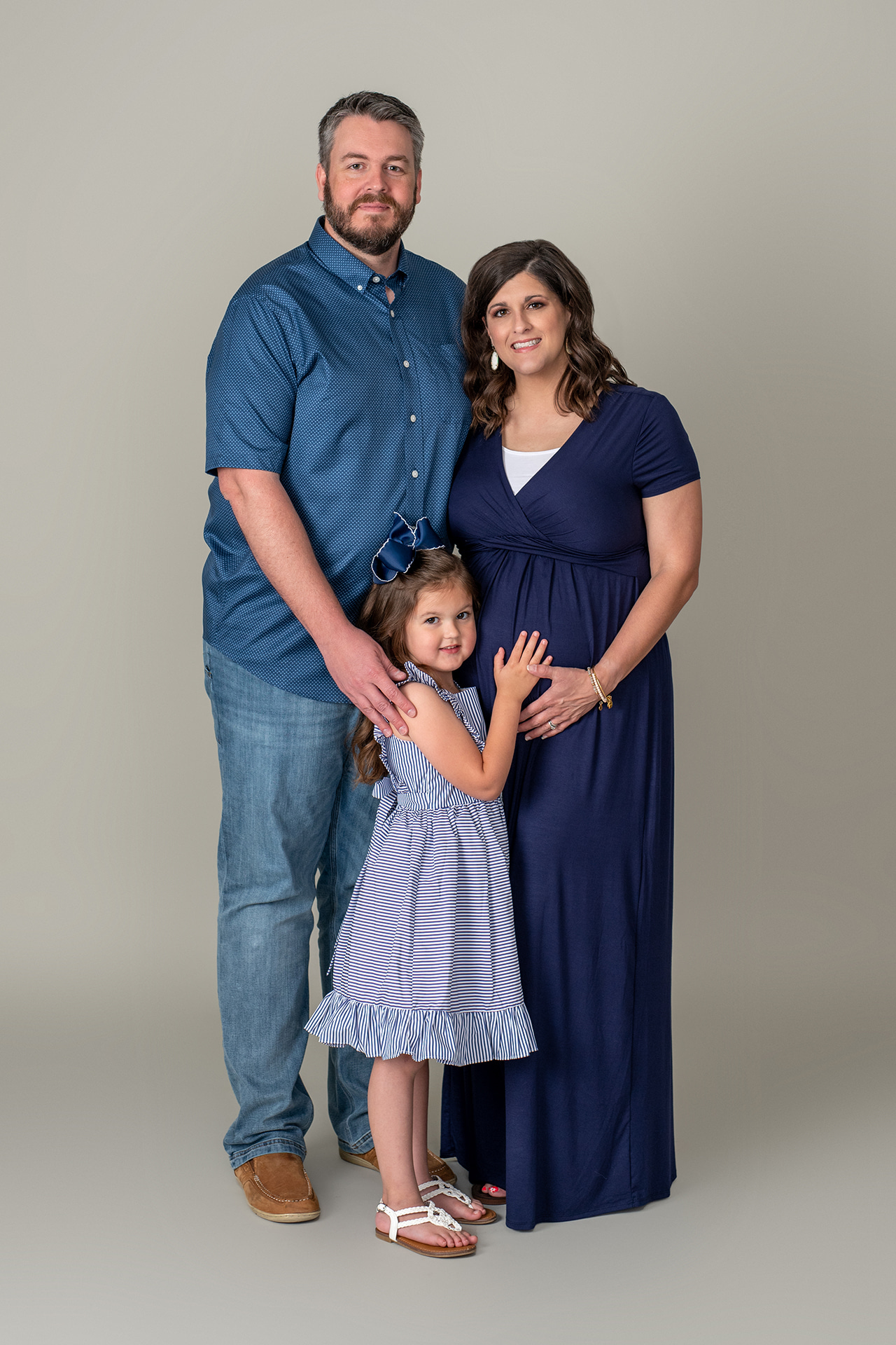 Mom, dad, and child holding mom's baby bump dressed in blue