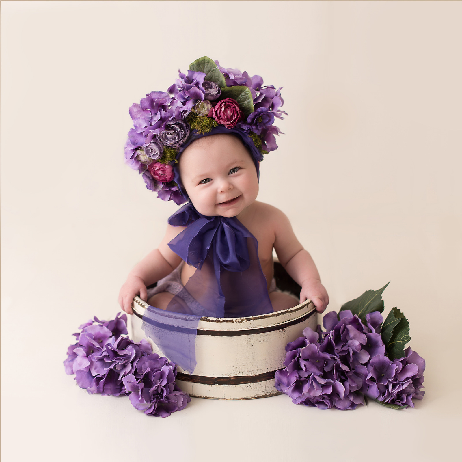 baby girl in purple flower hat sitting in a wooden tub
