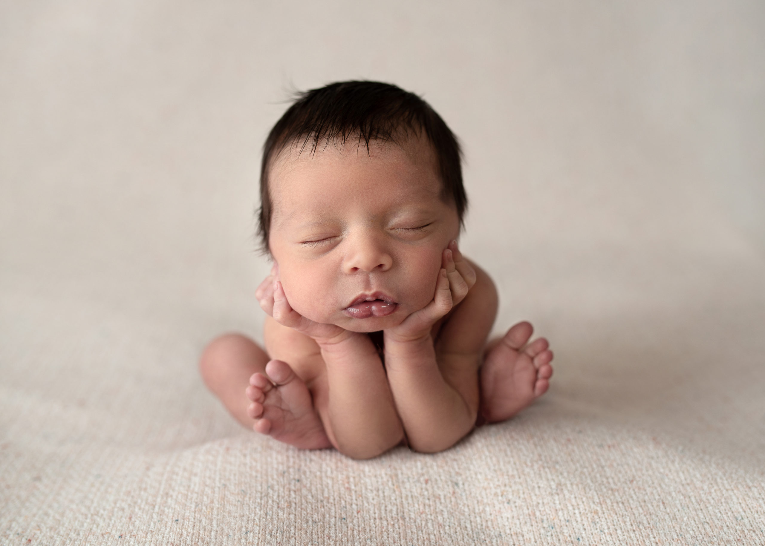 newborn baby with dark hair resting their head on their hands Houston Baby Stores