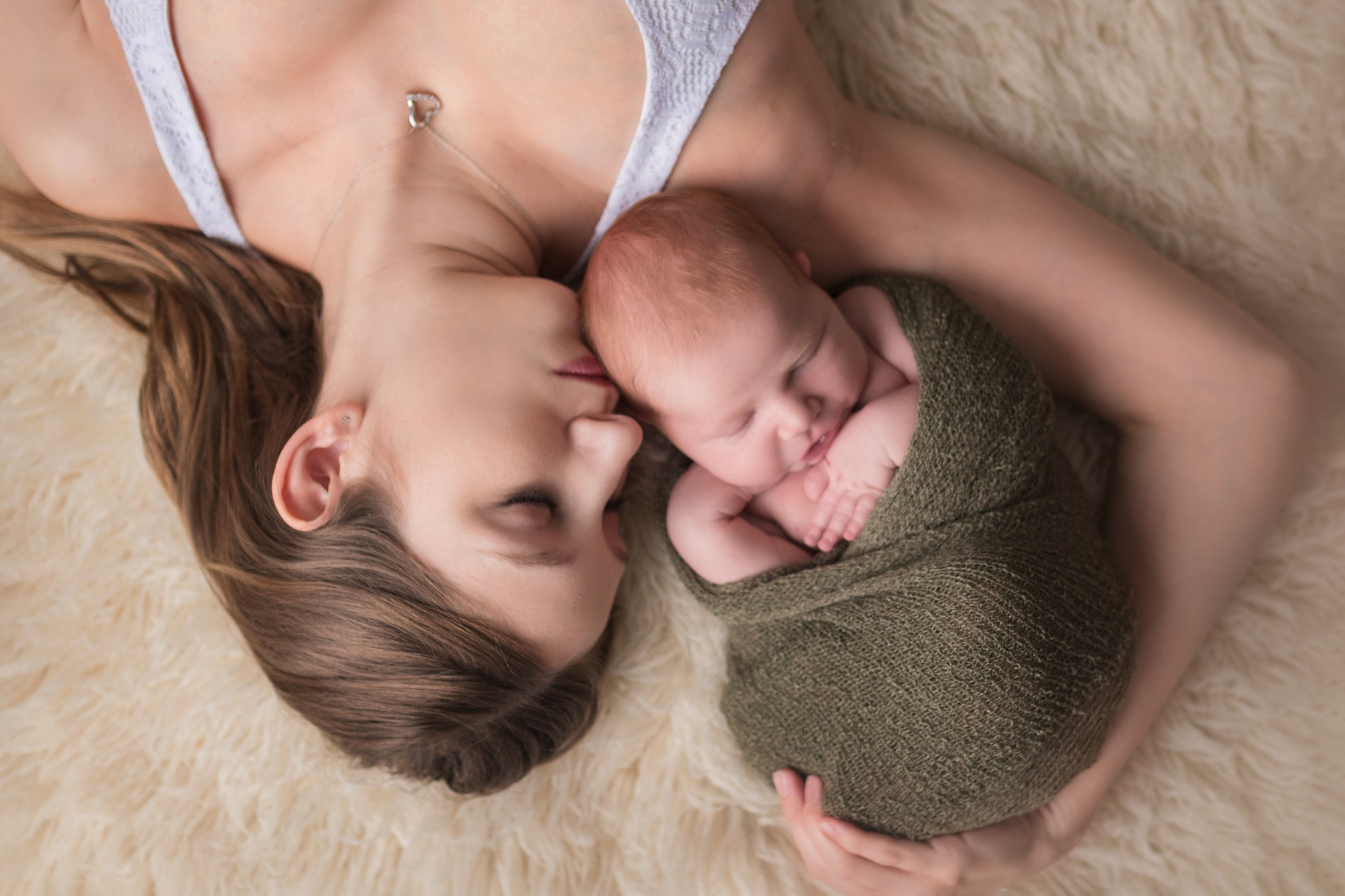 new mom laying on the floor with her newborn wrapped in green Houston Postpartum Doulas