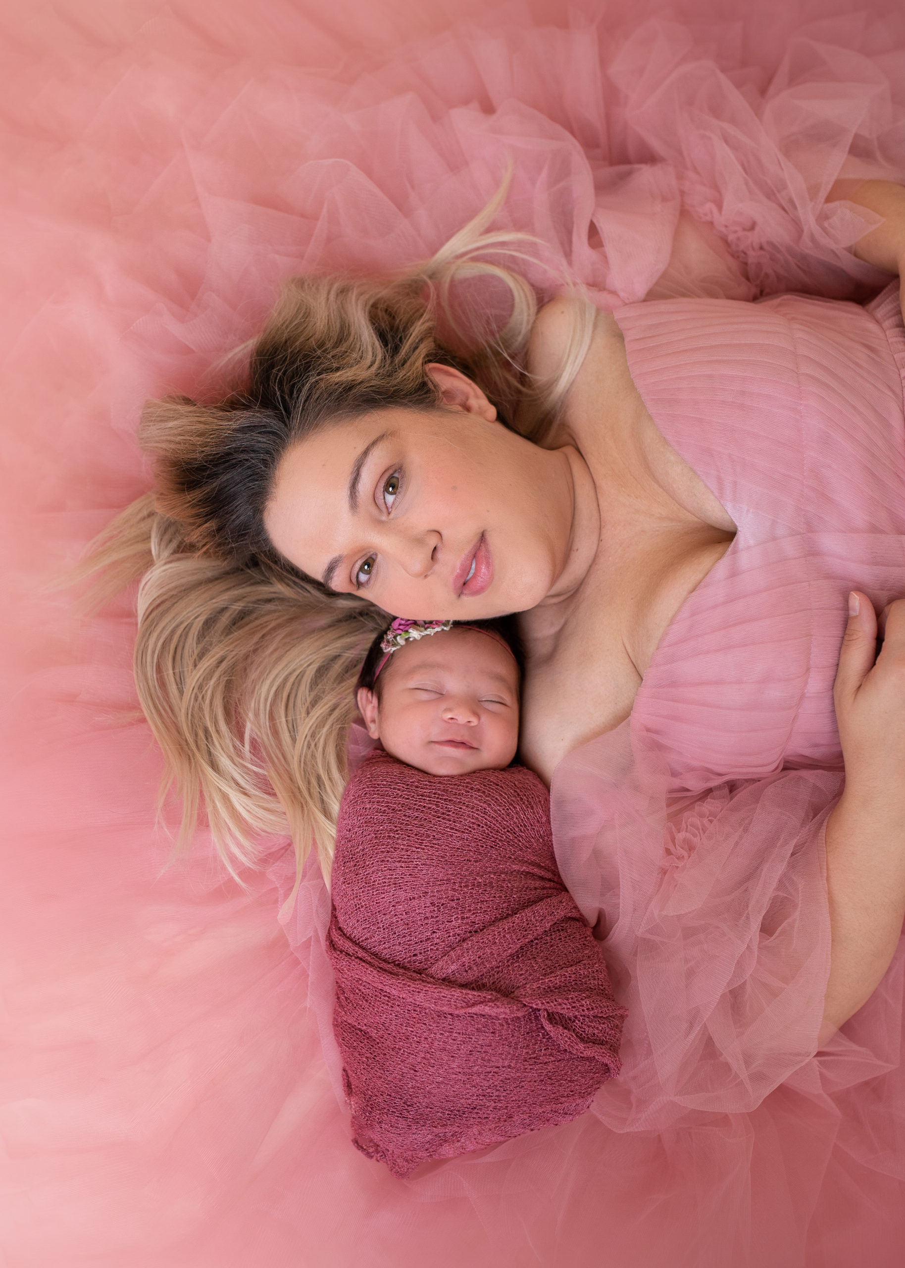 new mom laying on a pink backdrop with her newborn baby girl wrapped in shades of pink 3D Ultrasound League City