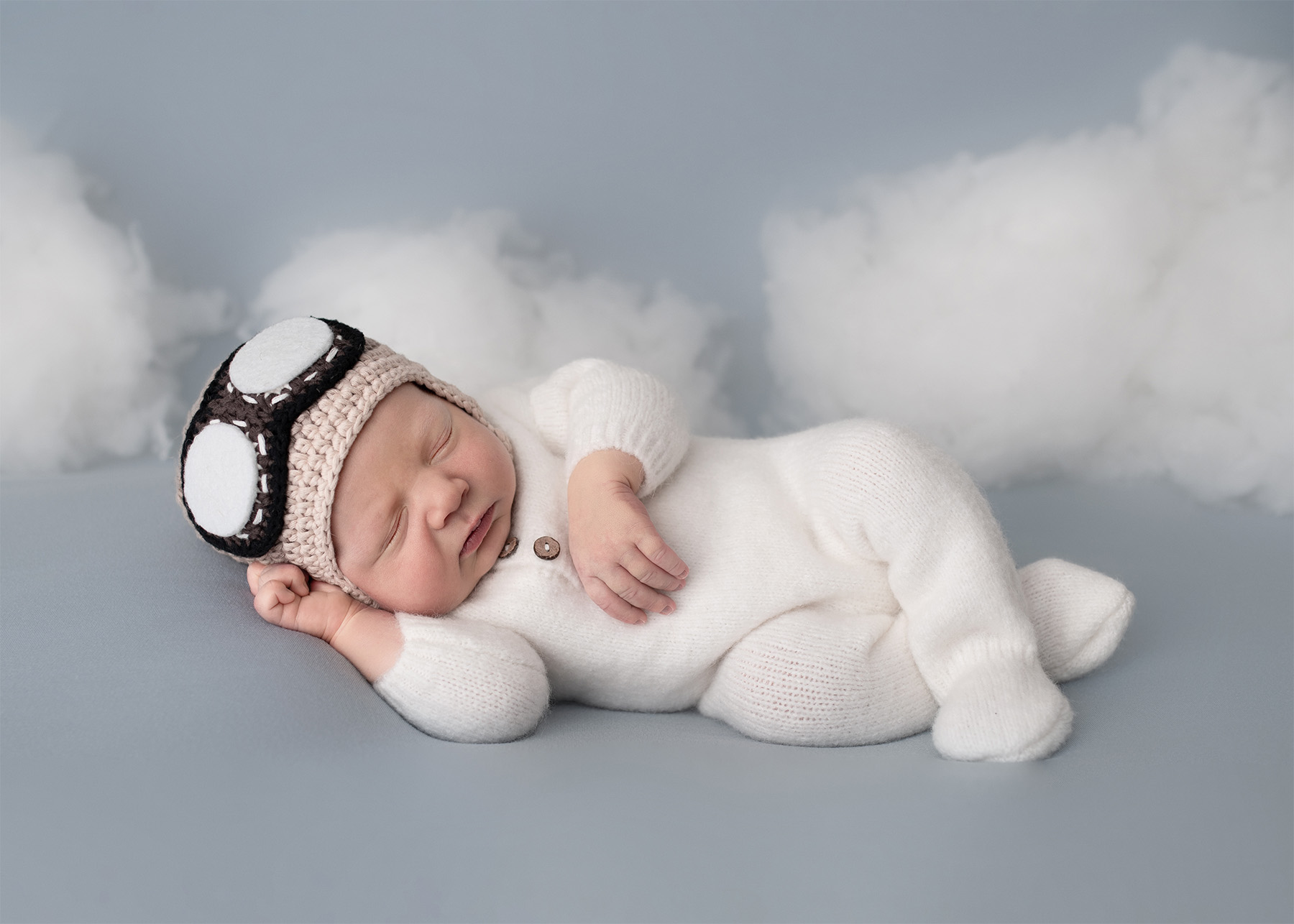 newborn baby in white laying on his side with clouds behind him Rockabye Baby Rentals