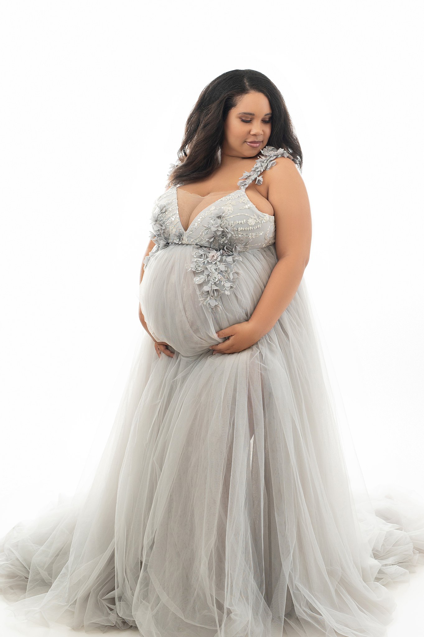 Mother to be stands in a studio looking down her shoulder in a grey maternity gown Houston home birth