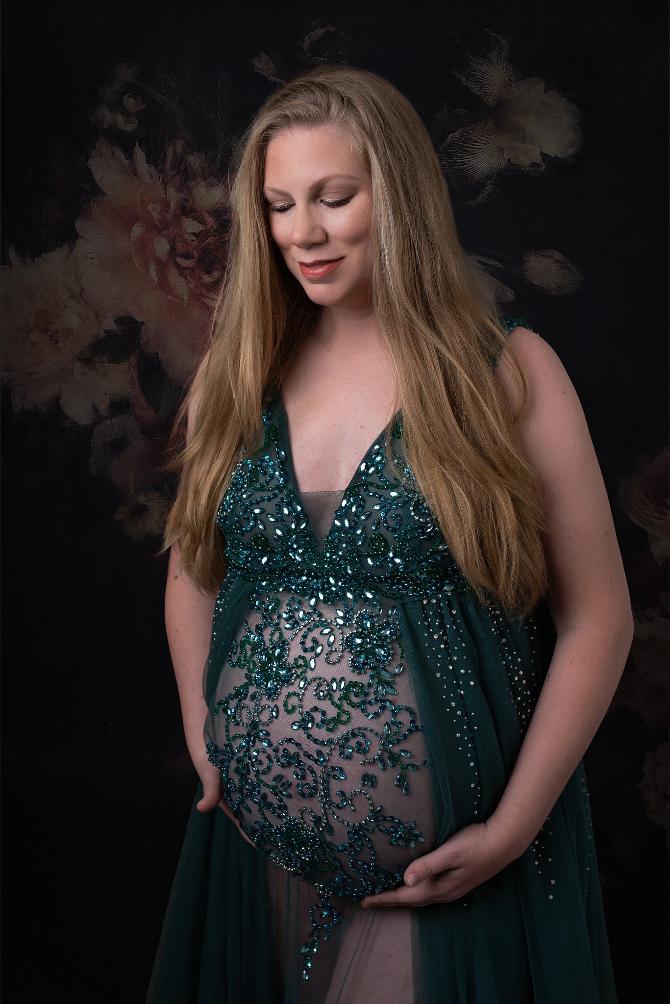 Mother to be holds her bump wearring a green lace maternity gown in a studio Texas Childrens Pavilion