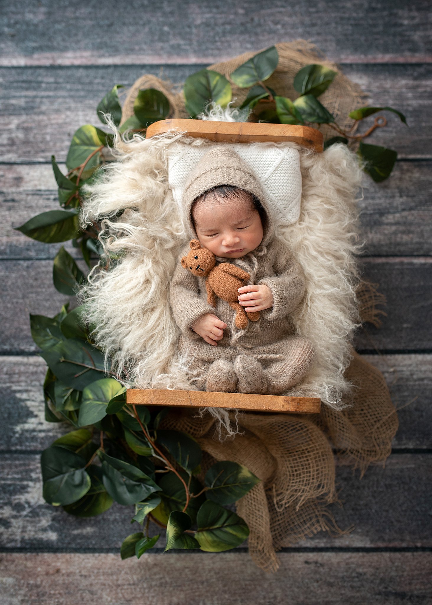 newborn baby wears a brown knit onesie while cuddling a teddy bear in a wooden bed The Children's place in Houston