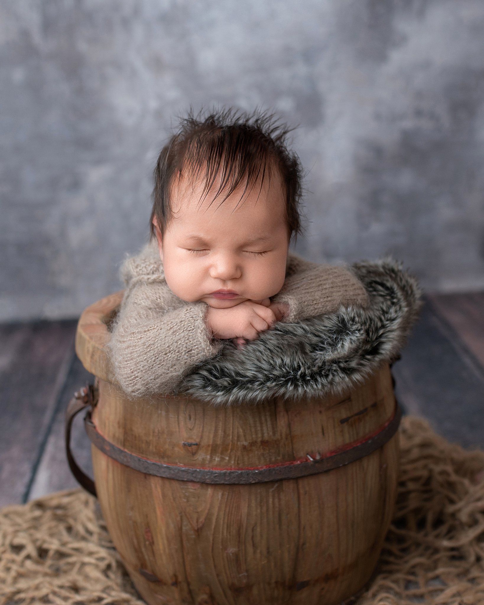 a newborn baby sleeps in a wooden bucket leaning on it's hands baby furniture stores in Houston