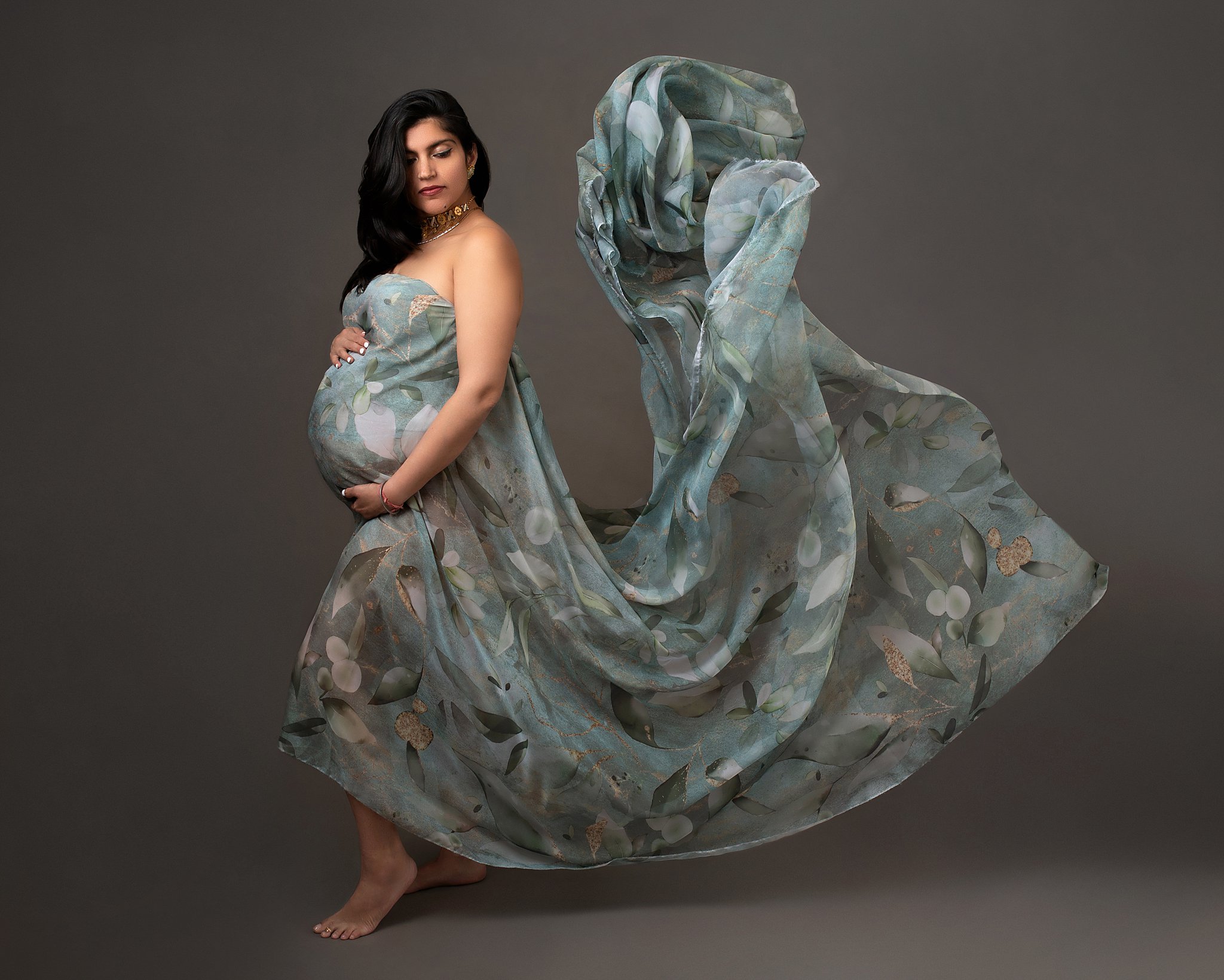 Mother to be in a blue floral pattern maternity gown stands in a studio with a long flowing train homebirth experience
