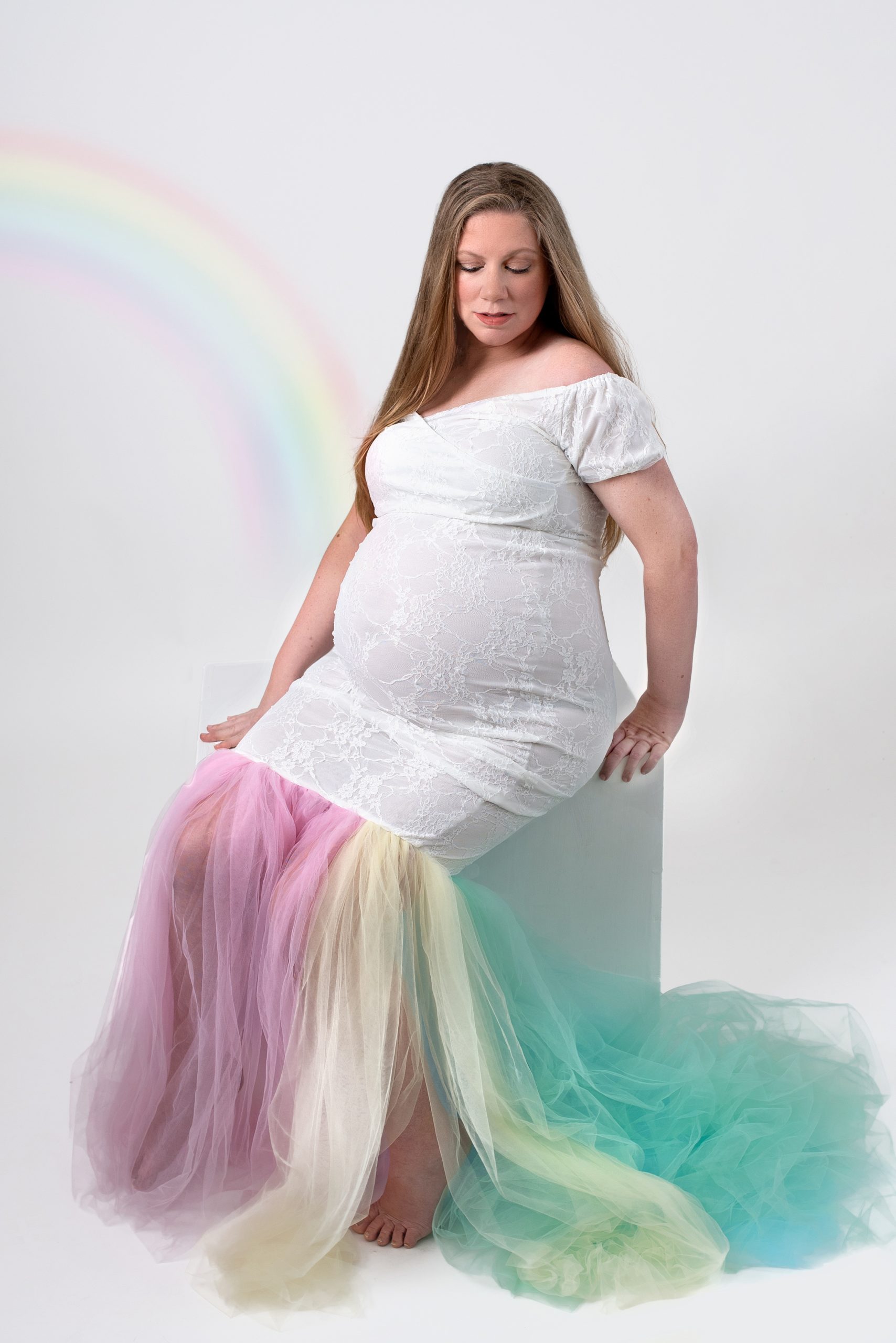 woman in a colorful maternity gown sits on a white cube in a studio houston midwives